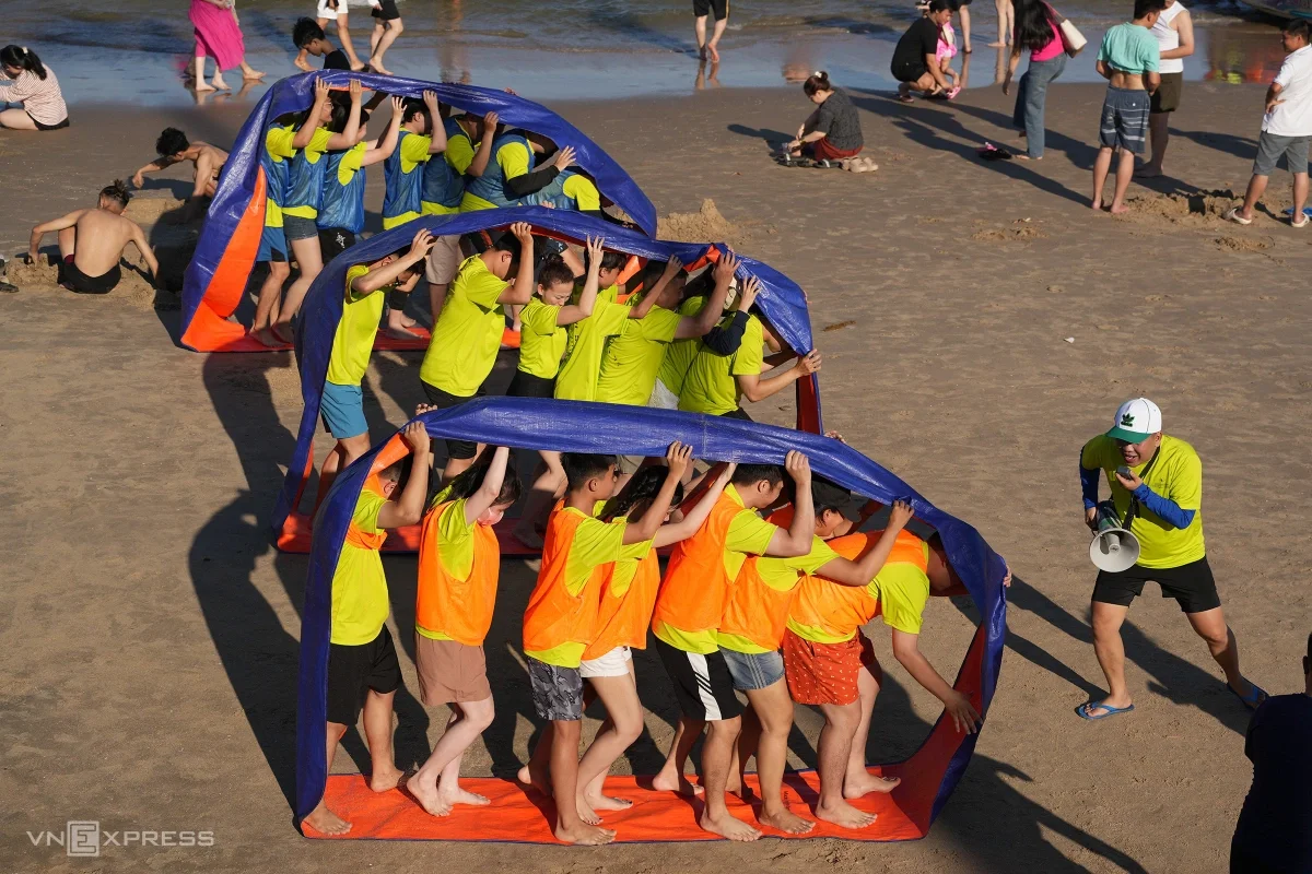 Nhóm nhân viên tham gia trò chơi "bước chân đồng đội" trên bãi cát gần quảng trường Cột Cờ.